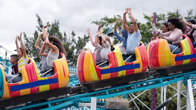 Happy group of people having fun in an amusement park riding on a rollercoaster with arms up